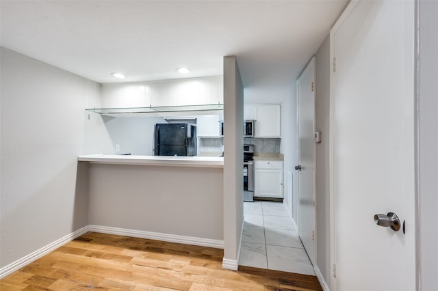 kitchen featuring stove, black fridge, white cabinets, backsplash, and light hardwood / wood-style floors