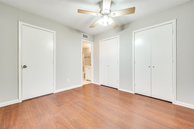 unfurnished bedroom featuring light hardwood / wood-style flooring, ceiling fan, and multiple closets