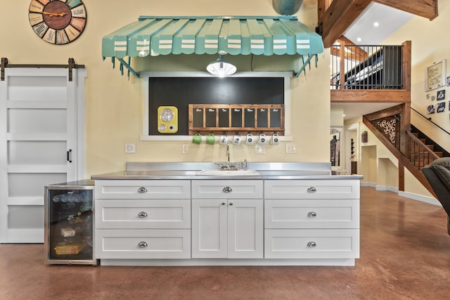 bar with white cabinetry, beverage cooler, sink, and a barn door