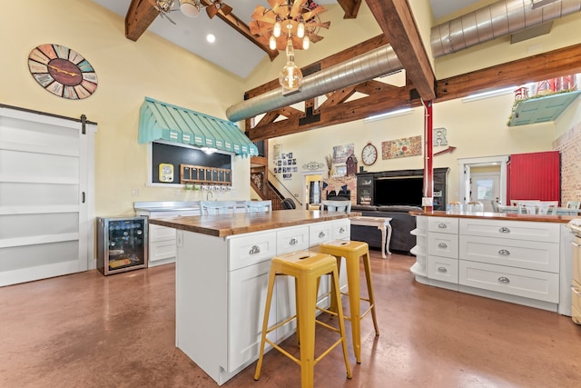 kitchen with a barn door, a kitchen breakfast bar, high vaulted ceiling, and white cabinetry