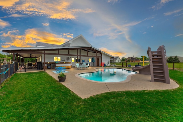 pool at dusk with a water slide, a lawn, outdoor lounge area, and a patio