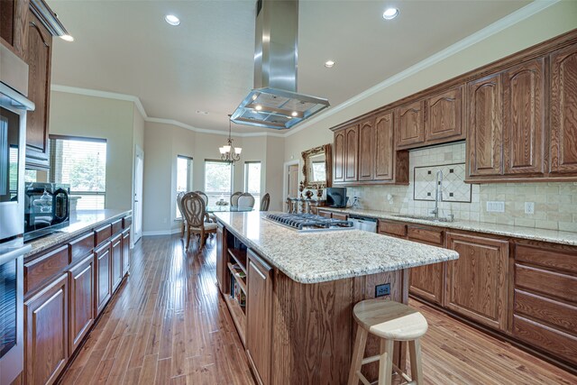 kitchen featuring decorative light fixtures, island range hood, backsplash, a kitchen island, and light hardwood / wood-style floors