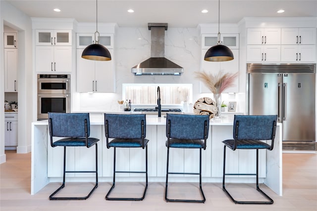 kitchen featuring light hardwood / wood-style flooring, stainless steel appliances, backsplash, white cabinetry, and wall chimney exhaust hood