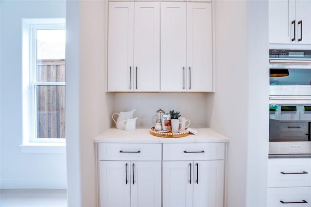 bar featuring white cabinetry, light stone countertops, and stainless steel double oven