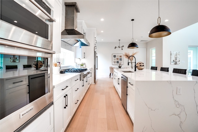 kitchen featuring light stone countertops, light hardwood / wood-style floors, decorative light fixtures, wall chimney exhaust hood, and sink