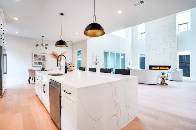 kitchen featuring light hardwood / wood-style flooring, an island with sink, a tile fireplace, sink, and white cabinets