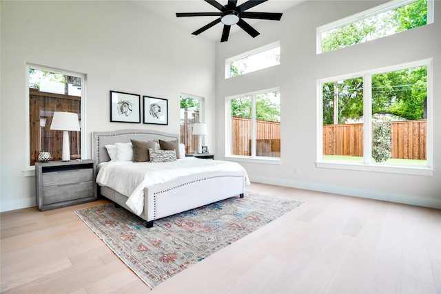 bedroom featuring a high ceiling, ceiling fan, multiple windows, and light hardwood / wood-style flooring