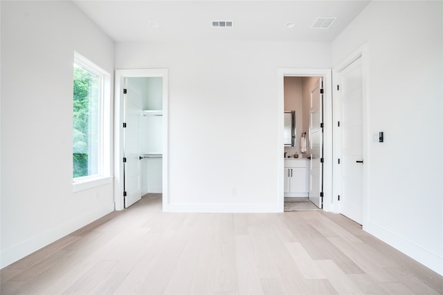 unfurnished bedroom with connected bathroom, light hardwood / wood-style flooring, a walk in closet, and multiple windows