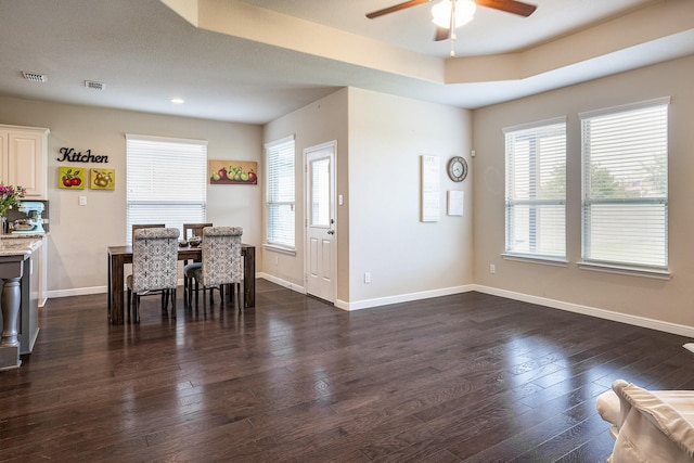 dining area with visible vents, baseboards, dark wood-style floors, a tray ceiling, and a ceiling fan