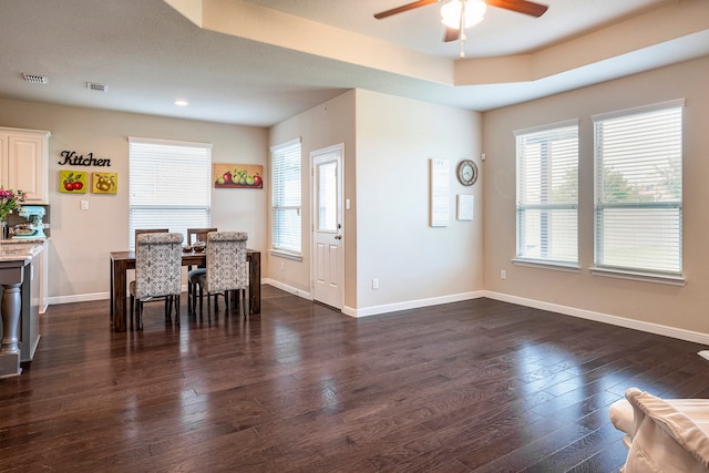 dining space with ceiling fan, a textured ceiling, dark hardwood / wood-style flooring, and a raised ceiling