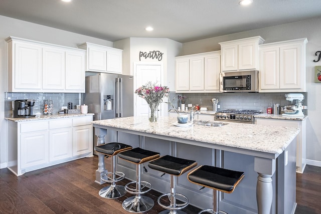 kitchen with decorative backsplash, appliances with stainless steel finishes, a sink, dark wood-style floors, and white cabinetry