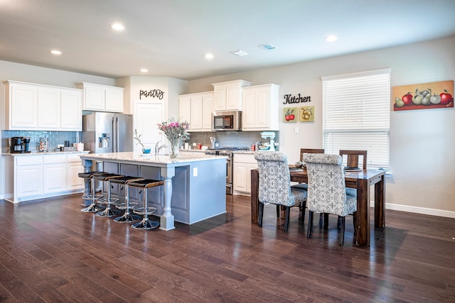 kitchen featuring stainless steel appliances, white cabinets, decorative backsplash, a kitchen island with sink, and dark wood-type flooring