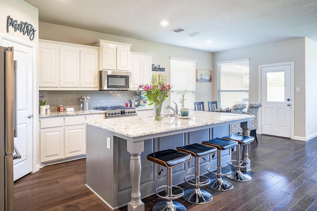 kitchen featuring appliances with stainless steel finishes, a breakfast bar area, dark wood finished floors, white cabinetry, and visible vents
