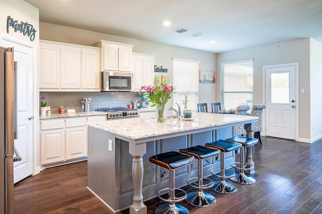 kitchen with white cabinets, dark hardwood / wood-style floors, light stone countertops, and appliances with stainless steel finishes