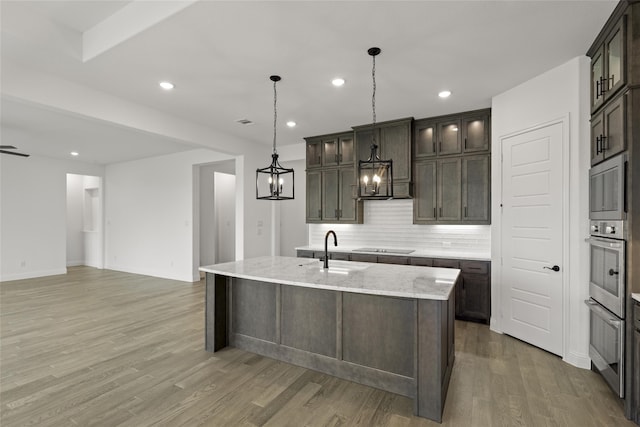 kitchen with a center island with sink, hanging light fixtures, dark brown cabinets, and wood-type flooring