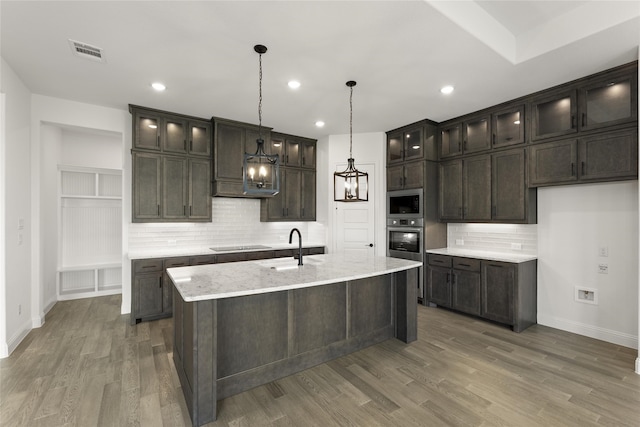 kitchen featuring black electric stovetop, light stone countertops, pendant lighting, oven, and a kitchen island with sink