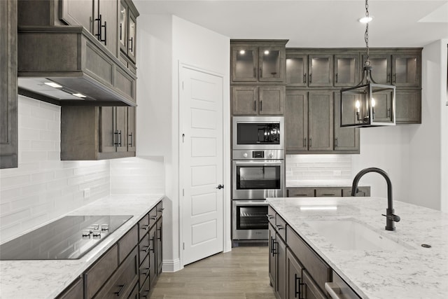 kitchen featuring appliances with stainless steel finishes, hanging light fixtures, wood-type flooring, light stone countertops, and sink