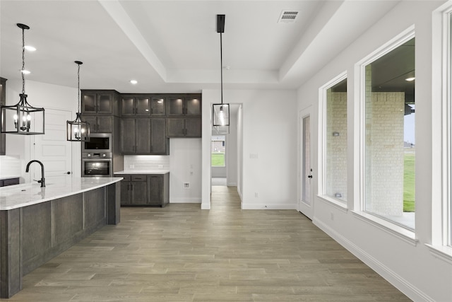 kitchen featuring built in microwave, stainless steel oven, hanging light fixtures, dark brown cabinetry, and light stone counters