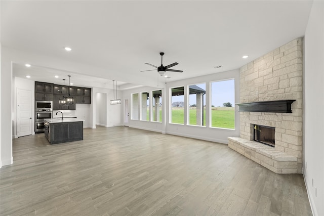 unfurnished living room featuring ceiling fan, hardwood / wood-style floors, and a stone fireplace