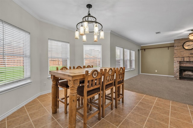 dining space with ceiling fan with notable chandelier, a stone fireplace, ornamental molding, and light tile patterned floors