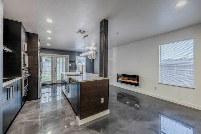 kitchen with french doors, a center island with sink, a fireplace, decorative light fixtures, and stainless steel appliances