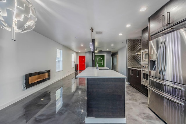 kitchen with appliances with stainless steel finishes, backsplash, ceiling fan, sink, and a center island with sink