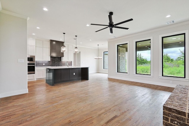 kitchen with a spacious island, white cabinetry, hanging light fixtures, stainless steel microwave, and plenty of natural light