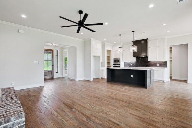 kitchen with decorative light fixtures, a center island with sink, ornamental molding, white cabinets, and backsplash