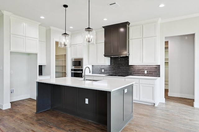 kitchen featuring premium range hood, sink, ornamental molding, appliances with stainless steel finishes, and a kitchen island with sink