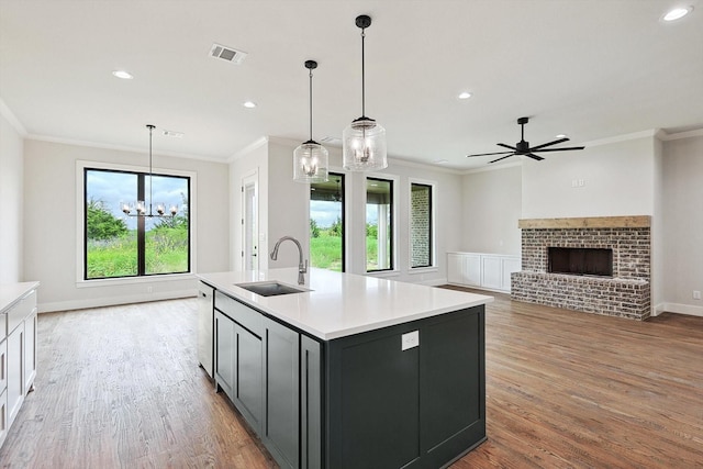 kitchen featuring a fireplace, wood-type flooring, sink, hanging light fixtures, and a kitchen island with sink