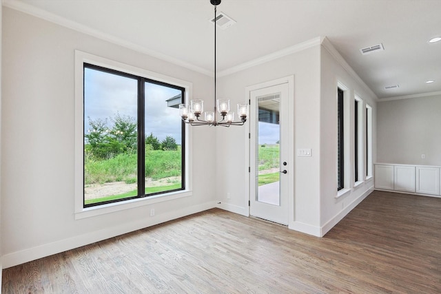 unfurnished dining area with hardwood / wood-style floors, a notable chandelier, ornamental molding, and a healthy amount of sunlight