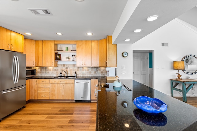 kitchen with stainless steel appliances, sink, hardwood / wood-style flooring, tasteful backsplash, and dark stone counters