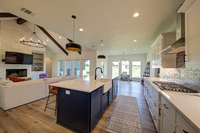 kitchen with wall chimney range hood, a large fireplace, beam ceiling, and white cabinets