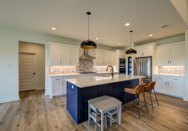 kitchen with appliances with stainless steel finishes, light hardwood / wood-style floors, tasteful backsplash, and wall chimney exhaust hood