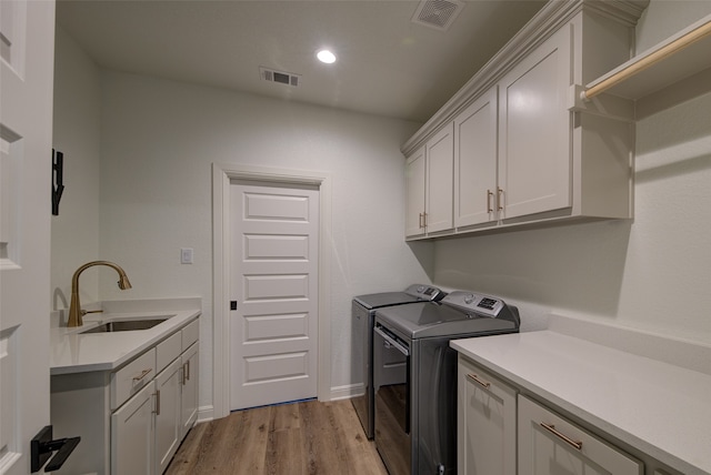 laundry area with sink, light hardwood / wood-style floors, washer and clothes dryer, and cabinets