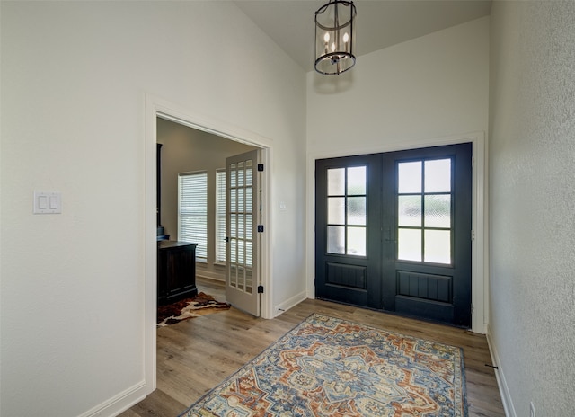 foyer entrance with french doors, lofted ceiling, wood-type flooring, and an inviting chandelier