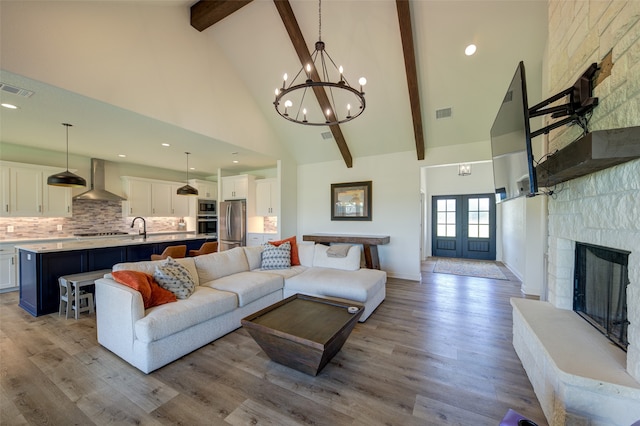 living room featuring beam ceiling, high vaulted ceiling, a stone fireplace, and light hardwood / wood-style flooring