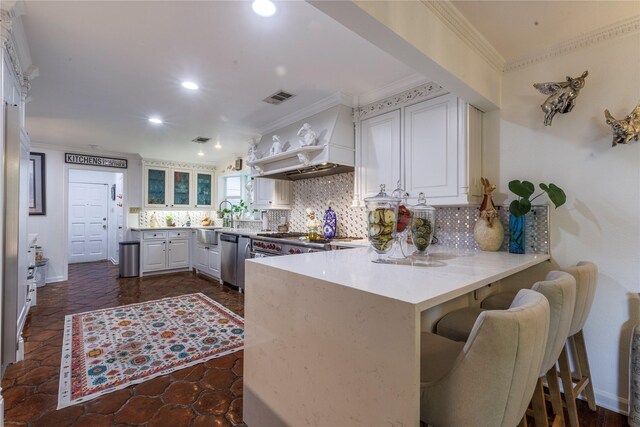 kitchen with kitchen peninsula, white cabinets, backsplash, appliances with stainless steel finishes, and ornamental molding