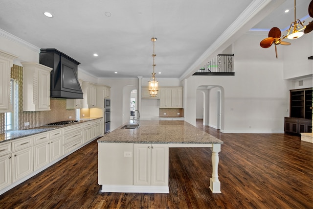 kitchen featuring dark wood-type flooring, hanging light fixtures, tasteful backsplash, and a center island with sink