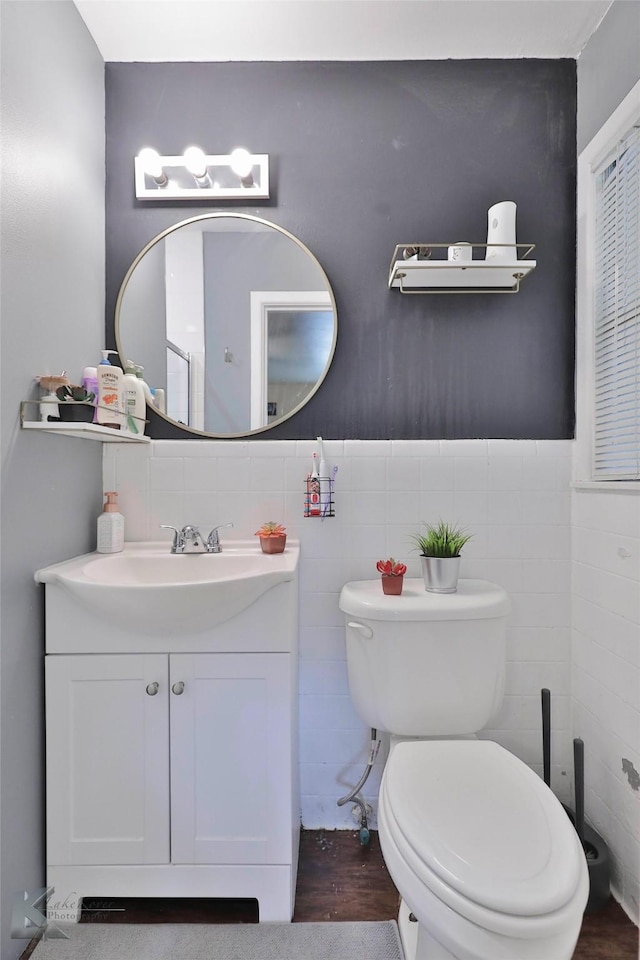 bathroom with wainscoting, toilet, wood finished floors, vanity, and tile walls