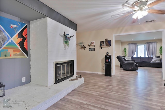 living room featuring ceiling fan, light hardwood / wood-style floors, and a brick fireplace