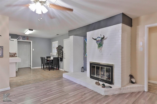 living area with a brick fireplace, ceiling fan, baseboards, and wood finished floors