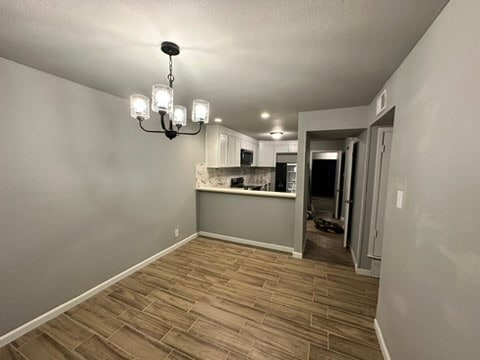 kitchen with wood-type flooring, hanging light fixtures, white cabinets, a chandelier, and tasteful backsplash