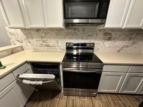 kitchen with backsplash, hardwood / wood-style flooring, white cabinets, and stainless steel electric range