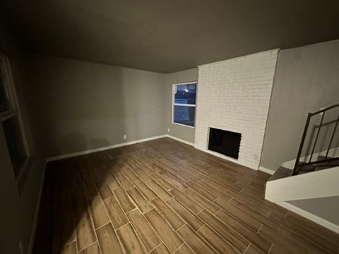 unfurnished living room featuring a fireplace, hardwood / wood-style flooring, and brick wall