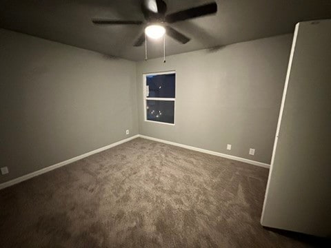 empty room featuring ceiling fan and dark carpet