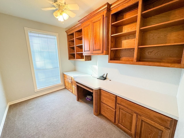 unfurnished office with light colored carpet, ceiling fan, and built in desk