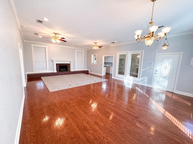 unfurnished living room with a brick fireplace, crown molding, ceiling fan with notable chandelier, and dark hardwood / wood-style floors