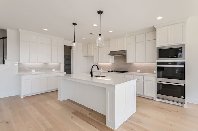 kitchen with white cabinets, sink, a center island with sink, and backsplash