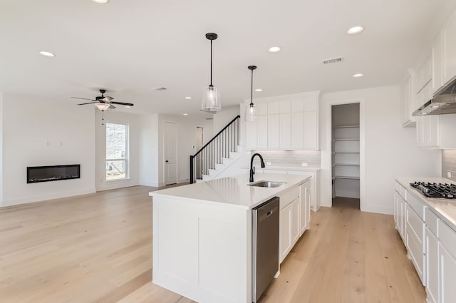 kitchen featuring a kitchen island with sink, backsplash, sink, white cabinetry, and appliances with stainless steel finishes